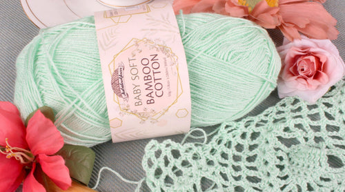 JubileeYarn Baby Soft Bamboo Cotton Yarn Green Mint color yarn ball laying next to crocheted doily and pink flowers